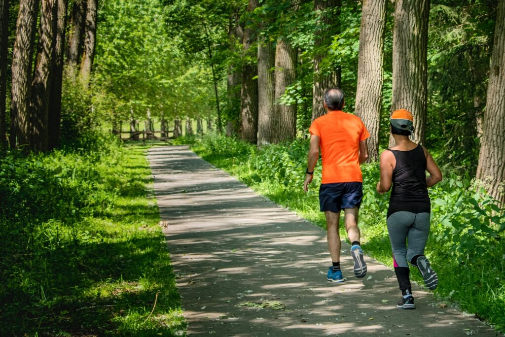 man in orange t-shirt and gray pants with blue shoes walking on pathway