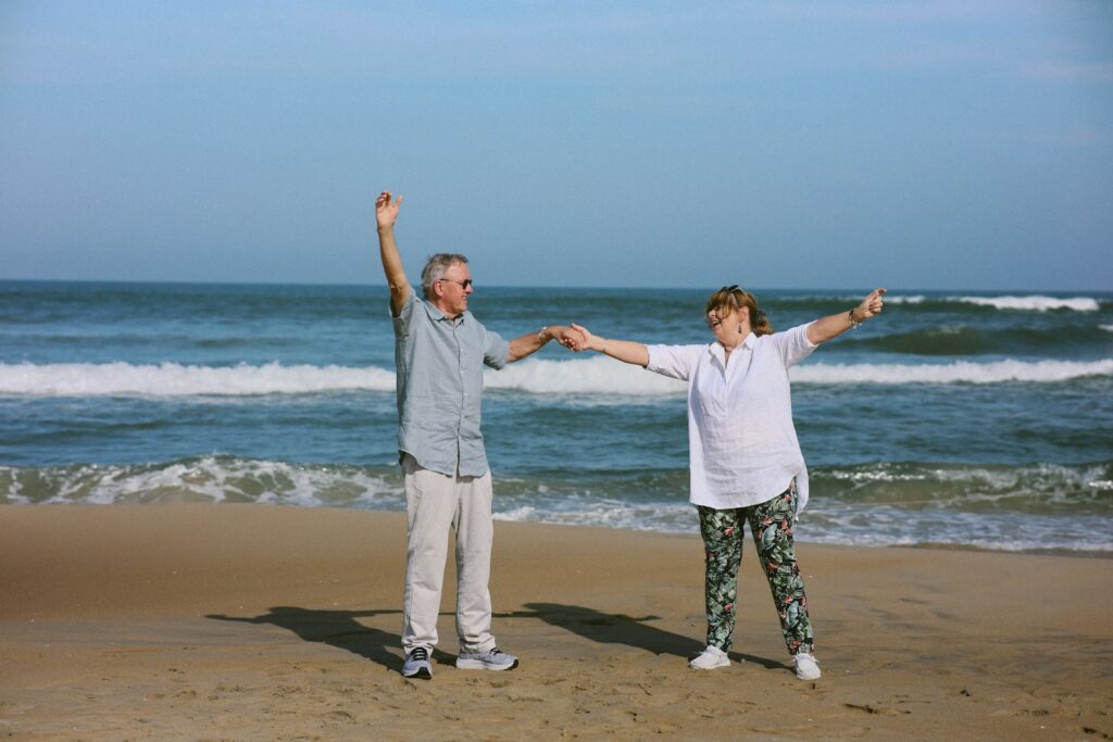 Elderly couple dancing on a beach with ocean waves.