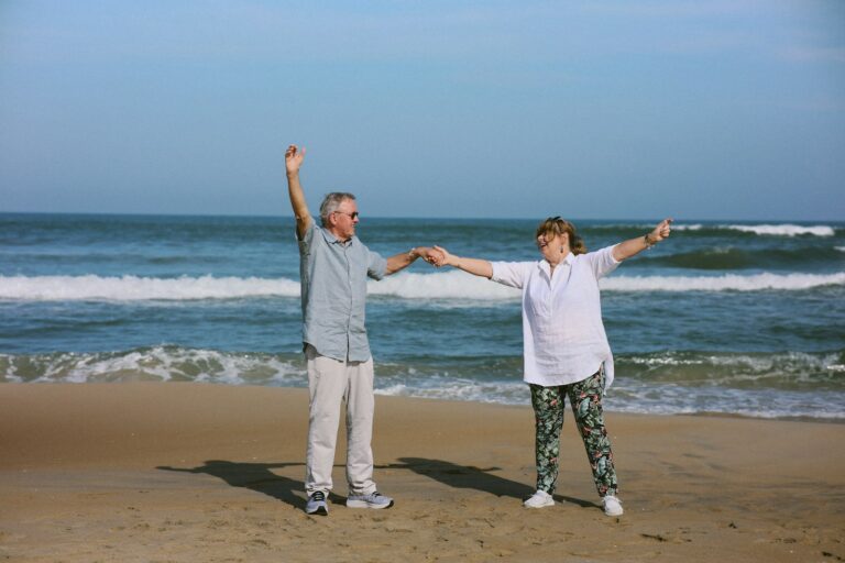 Elderly couple dancing on a beach with ocean waves.